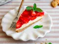 Ein Stück Erdbeerkuchen ohne Backen, mit frischen Erdbeeren und Minze garniert, auf einem weißen Teller.