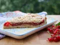 Ein Stück saftiger Johannisbeer Streuselkuchen mit frischen roten Johannisbeeren daneben.
