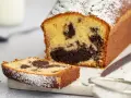 Ein saftiger Marmorkuchen in Kastenform, bestäubt mit Puderzucker. Eine Scheibe liegt daneben, bereit zum Genuss.