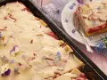 Saftiger Rhabarberkuchen mit Quark, dekoriert mit Veilchen und Vergissmeinnicht. Ein Stück ist auf einem Teller angerichtet.