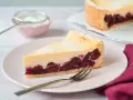 Ein saftiges Stück Kirsch Schmand Kuchen mit cremigem Belag und Kirschen auf Mürbeteigboden, bestäubt mit Puderzucker.