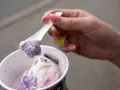 Eine Hand mit pink lackierten Nägeln hält einen Löffel mit zwei Kugeln Eis im Becher, italienisch.