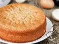 Perfekter Biskuitboden: Ein goldbrauner Kuchen, bereit für Ihr nächstes biskuitboden rezept. Eier und Schneebesen deuten auf die Zubereitung hin.