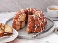 Ein köstlicher Monkey Bread mit Zimt und Zuckerguss, bereit zum Teilen. Daneben eine Tasse Kaffee und Zimtstangen.