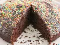 Ein saftiger, veganer Kuchen mit Schokoladenglasur und bunten Streuseln. Ein Stück fehlt, was Lust auf mehr macht.