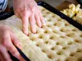 Hände drücken Vertiefungen in den Teig für ein Butterkuchen Rezept. Würfel aus Butter liegen bereit.