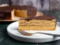 Ein Stück Schokoladen-Baumkuchen mit vielen Schichten liegt auf einem Teller. Das Baumkuchen Rezept ist ein Klassiker.