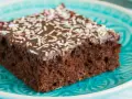 Ein Stück saftiger Schokoladen-Blechkuchen mit Schokoladenglasur und bunten Streuseln auf einem türkisfarbenen Teller. Ein einfaches Blechkuchen Rezept für Glücksmomente.