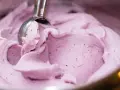 Ein Löffel nimmt eine Portion cremiges, kalorienarmes Eis mit Beerenstücken auf.