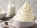 Cremiges Softeis in einer Schüssel, daneben Milch, Vanilleschoten und Löffel. Die Zutaten für das perfekte Softeis.