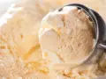 Ein Löffel nimmt eine Kugel cremiges Eis auf. Kleine eiskristalle im eis glitzern im Licht.