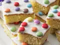Bunter Fantakuchen-Rezept: saftige Kuchenstücke mit weißer Glasur und bunten Smarties. Perfekt für Kindergeburtstage!