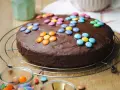 Schokokuchen mit bunten Smarties, perfekt für Kinder. Ein Glas mit weiteren Süßigkeiten steht daneben.