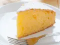 Ein saftiges Stück vanille kuchen, bestäubt mit Puderzucker, wartet auf einer weißen Platte mit einer Gabel.