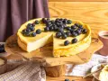 Ein köstlicher Skyr Kuchen, üppig belegt mit frischen Blaubeeren, wartet auf seine Genießer. Daneben eine Tasse Kaffee.