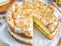 Ein köstlicher Stachelbeer Baiser Kuchen mit Biskuitböden, Sahne und Mandelsplittern. Ein Stück ist bereits herausgeschnitten.