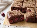 Saftiger kirschkuchen mit frischen kirschen, bestreut mit Nüssen. Daneben liegen frische Kirschen und Schokostückchen.