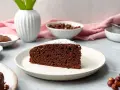Ein saftiges Stück **Nutella Kuchen** mit Puderzucker bestäubt, daneben Nüsse und eine Vase.