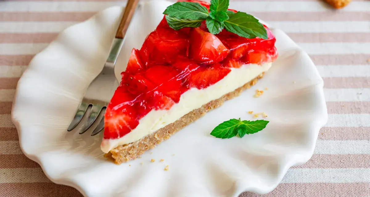 Ein Stück Erdbeerkuchen ohne Backen, mit frischen Erdbeeren und Minze garniert, auf einem weißen Teller.