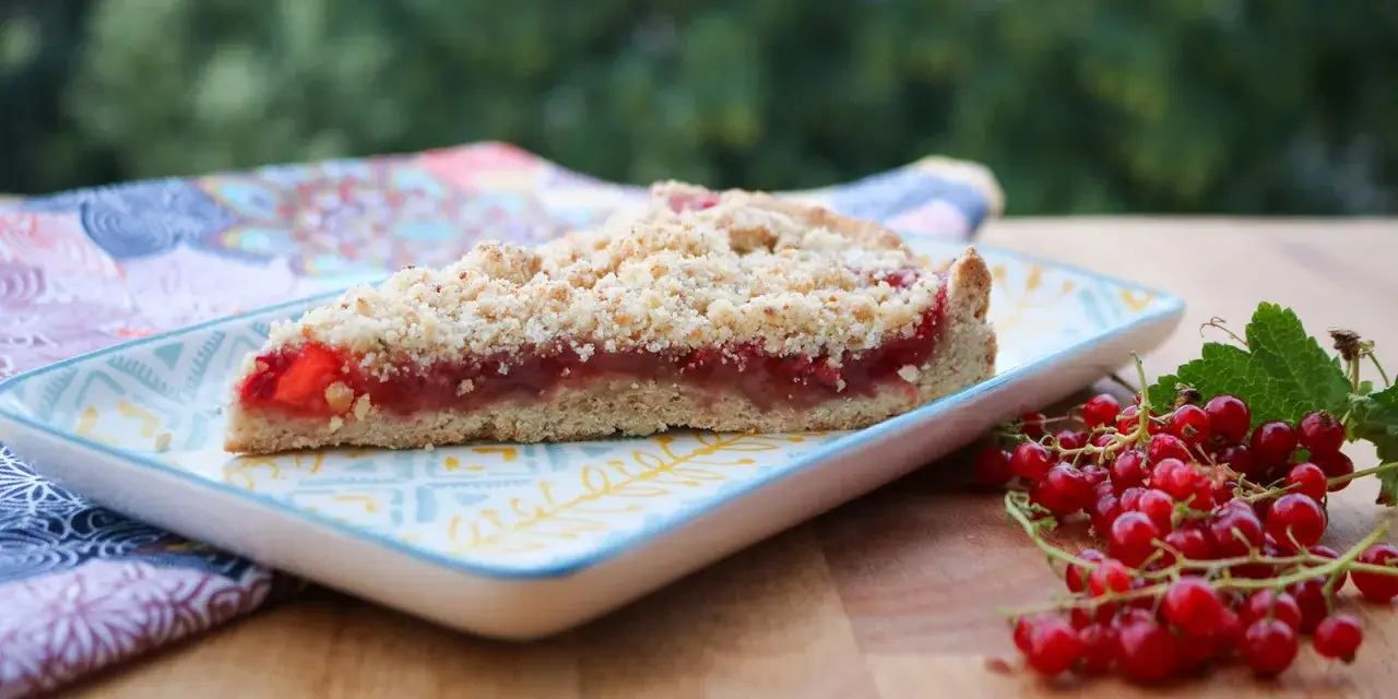 Ein Stück saftiger Johannisbeer Streuselkuchen mit frischen roten Johannisbeeren daneben.