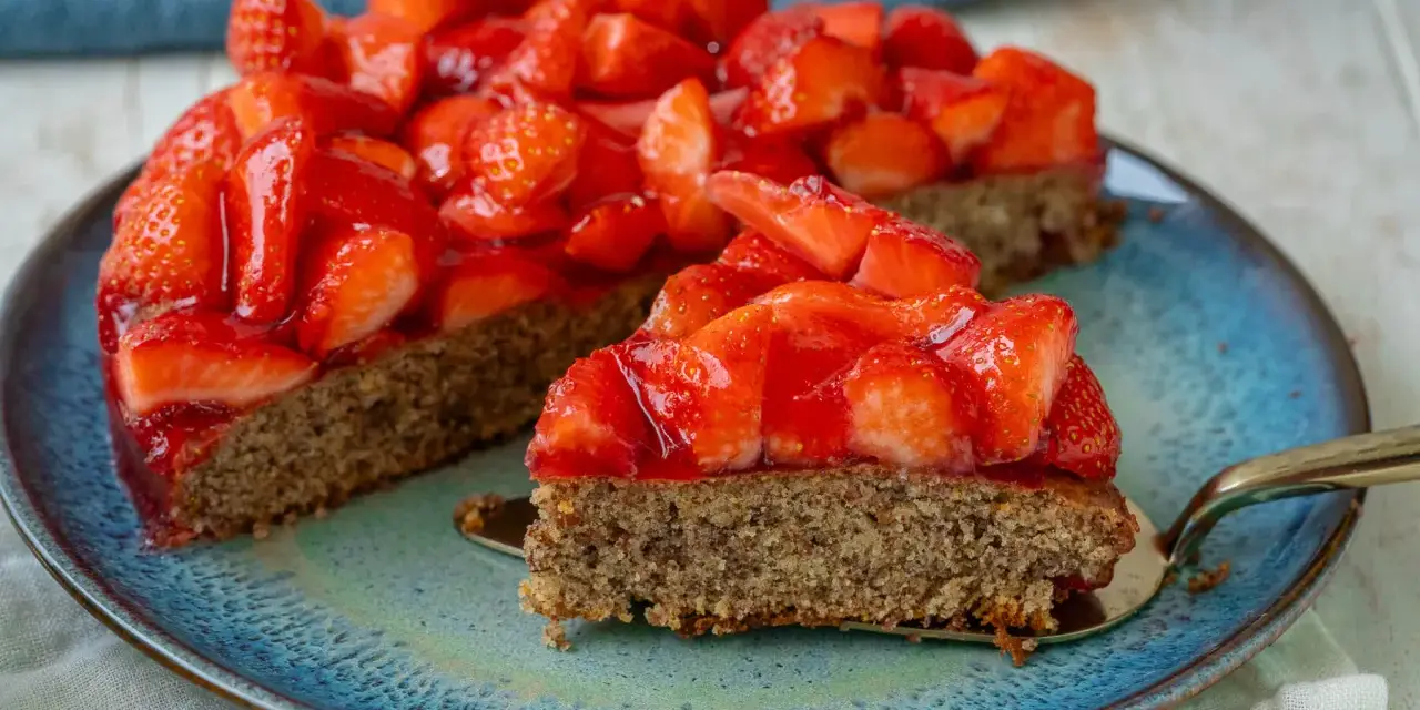 Ein saftiger glutenfreier Erdbeerkuchen mit frischen Erdbeeren und glänzender Tortenglasur auf einem blauen Teller.