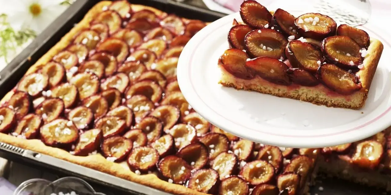 Ein saftiger Zwetschgenkuchen vom Blech, mit süßen Früchten und Zucker bestreut, wartet darauf, genossen zu werden.