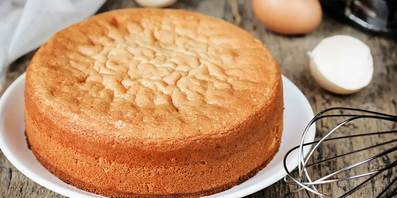 Perfekter Biskuitboden: Ein goldbrauner Kuchen, bereit für Ihr nächstes biskuitboden rezept. Eier und Schneebesen deuten auf die Zubereitung hin.