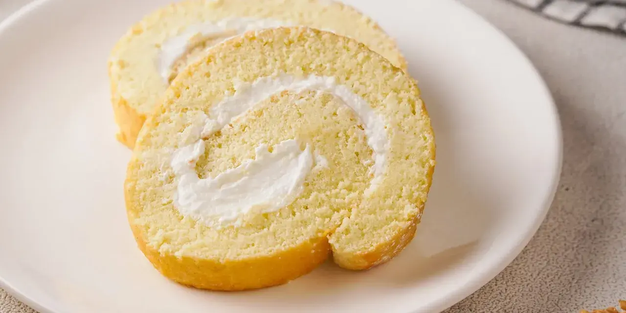 Zwei Scheiben einer leichten Biskuitrolle mit cremiger Füllung, perfekt für ein Zitronenrolle Rezept.