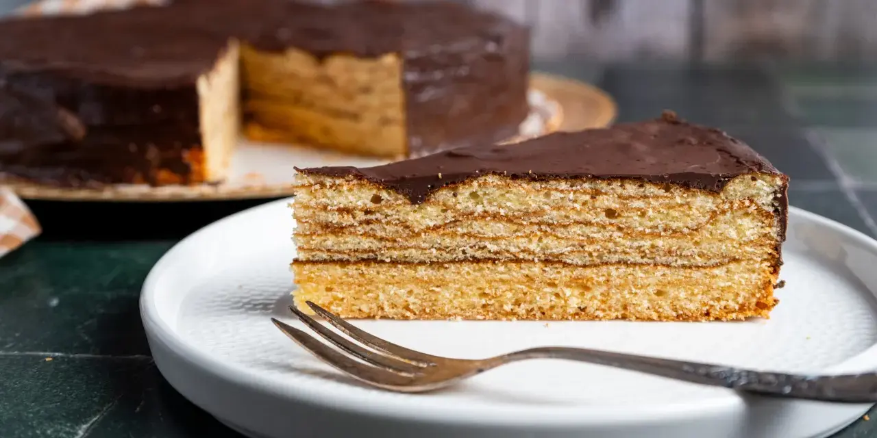 Ein Stück Schokoladen-Baumkuchen mit vielen Schichten liegt auf einem Teller. Das Baumkuchen Rezept ist ein Klassiker.