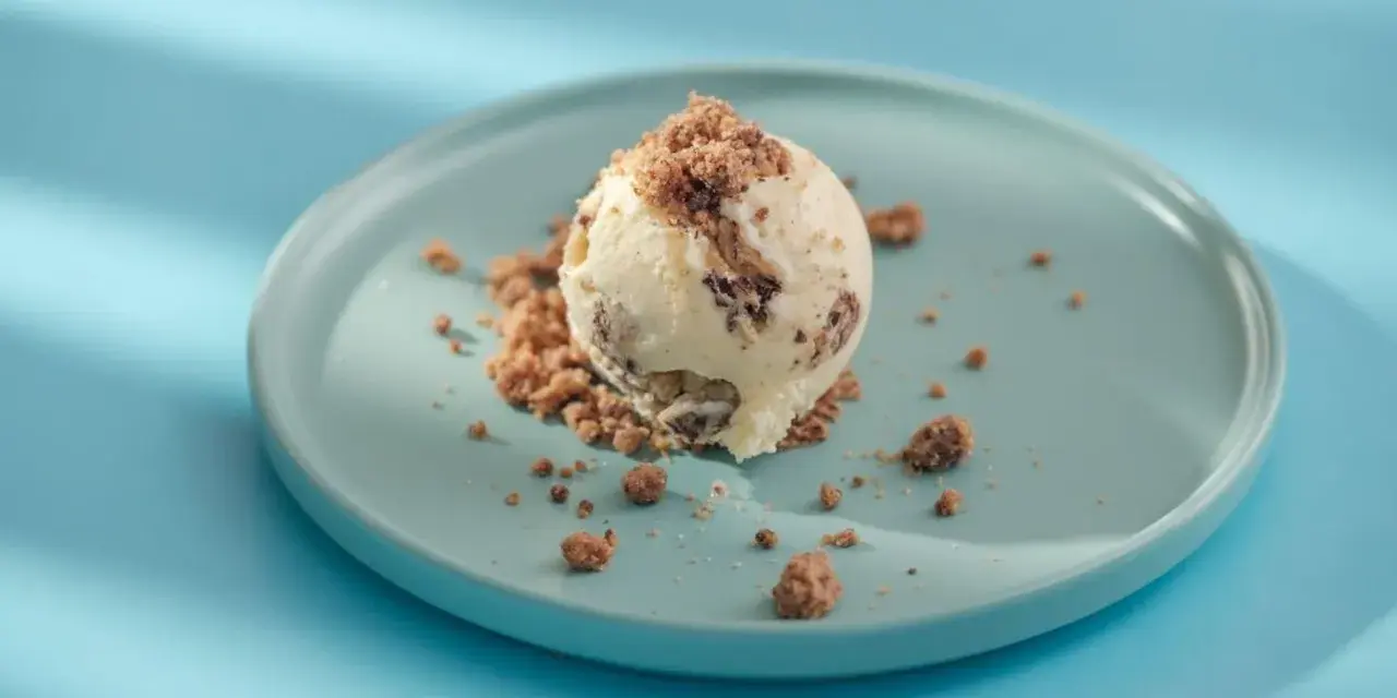 Eiscreme mit Schokoladenstückchen und Krümeln, serviert auf einem blauen Teller. Glukosesirup sorgt für die cremige Konsistenz.