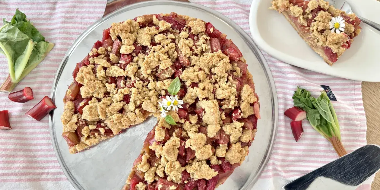 Ein köstlicher Rhabarberkuchen mit Streuseln, garniert mit Gänseblümchen. Frischer Rhabarber und knusprige Streusel machen diesen Kuchen zum Genuss.