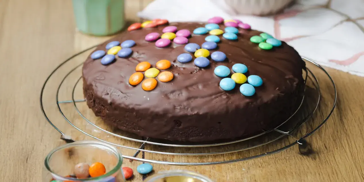 Schokokuchen mit bunten Smarties, perfekt für Kinder. Ein Glas mit weiteren Süßigkeiten steht daneben.