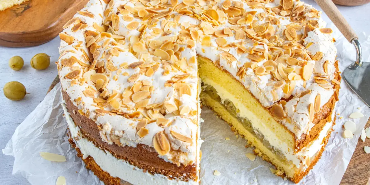 Ein köstlicher Stachelbeer Baiser Kuchen mit Biskuitböden, Sahne und Mandelsplittern. Ein Stück ist bereits herausgeschnitten.