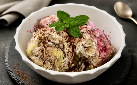 Schüssel mit Zuppa Inglese Gelato, garniert mit Minze und Schokoladenraspeln. Ein Löffel liegt daneben.