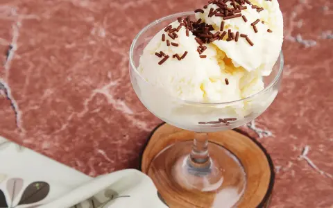 Cremiges Litschi Eis mit Schokostreuseln in einem Glas auf einem Holzuntersetzer.