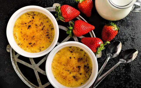 Zwei cremige Crème brûlée mit karamellisierter Kruste, garniert mit frischen Erdbeeren und einem Milchkännchen.