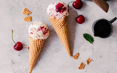 Zwei Waffelhörnchen mit Joghurt Kirsch Eis, garniert mit frischen Kirschen und Minze.
