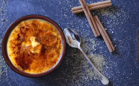 Cremige Crema Catalana mit karamellisierter Zuckerkruste, daneben Zimtstangen und Zucker.