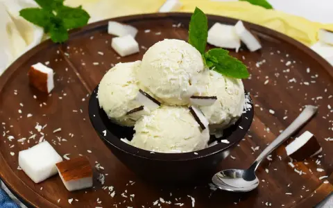 Schüssel mit cremigem Kokoseis, garniert mit Kokosraspeln und Minze. Perfekt, um Kokoseis selber zu machen!