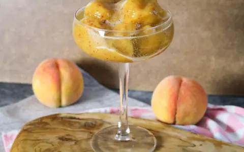 Erfrischendes Pfirsich-Prosecco-Sorbet in einem eleganten Glas, daneben reife Pfirsiche.