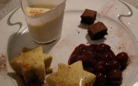 Sterne aus Zimtstern-Eis, garniert mit Kirschen und Brownies, serviert auf einem Teller.
