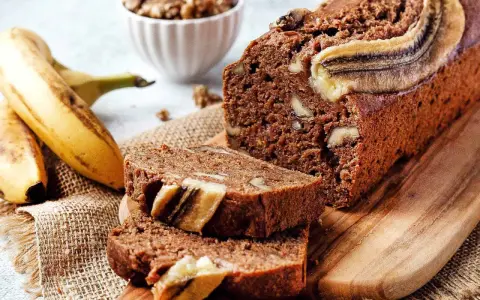 Saftiges, veganes Bananenbrot mit Walnüssen und Bananenscheiben, daneben frische Bananen und eine Schüssel Nüsse.