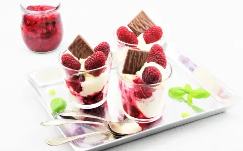 Drei Gläser mit cremigem Dessert, Himbeeren und Schokolade. Ein Glas mit Himbeermarmelade daneben. Schnelles Eis für den Sommer.