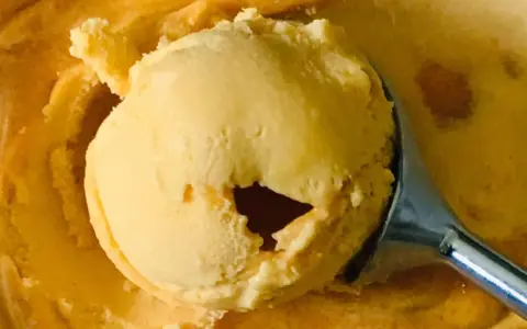 Ein Löffel hebt eine Kugel cremiges Sanddorn-Eis aus einer Schüssel. Die Farbe erinnert an die Sonne.