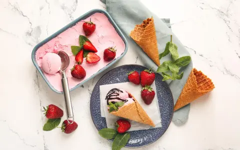 Ein Behälter mit rosa Obst Eis, Erdbeeren und Minze. Ein Eisbecher mit Eis und Schokoladensauce.