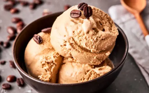 Kaffee Eis in einer Schale, garniert mit Kaffeebohnen. Ein Löffel liegt daneben.