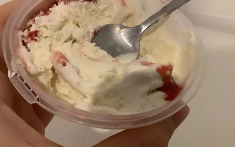 Ein Löffel steckt in einem Becher mit schmelzendem, altem Eis mit Erdbeersauce.