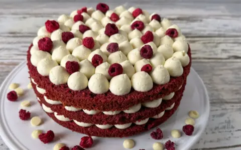 Ein mehrschichtiger Red Velvet Kuchen mit weißer Creme und Himbeeren.