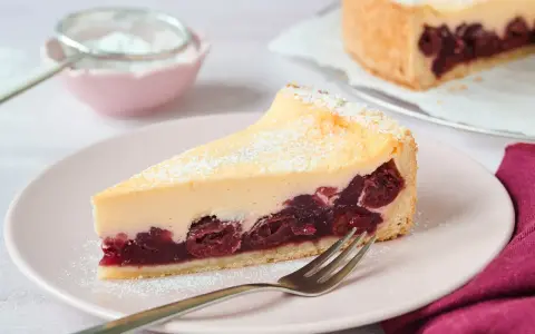 Ein saftiges Stück Kirsch Schmand Kuchen mit cremigem Belag und Kirschen auf Mürbeteigboden, bestäubt mit Puderzucker.