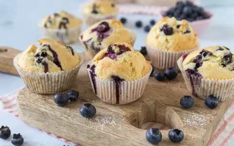 Saftige Blaubeer Muffins mit frischen Blaubeeren, auf einem Holzbrett arrangiert.